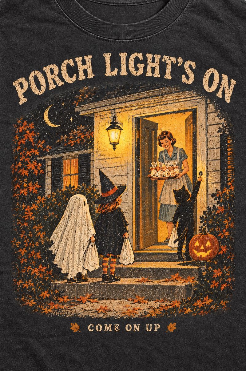 Washed black tee printed with trick-or-treaters on a front porch, a mom in the doorway with a tray of popcorn balls, words Porch Light’s On, Come On Up